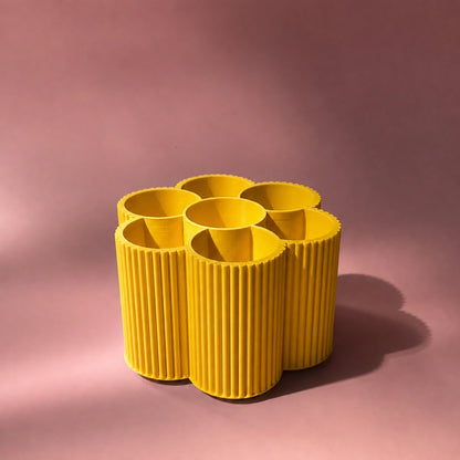 gelbe Stiftebox in Blumenform vor rosa Hintergrund