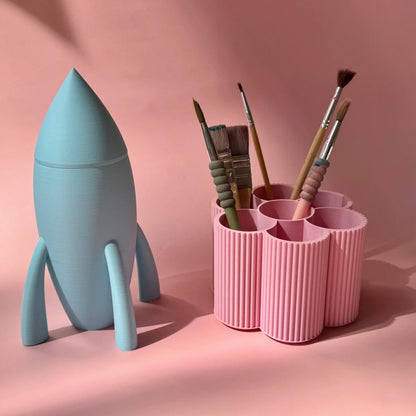 Stifteboxen Rakete in hellblau und Blume in rosa von tryk.design vor rosa Hintergrund